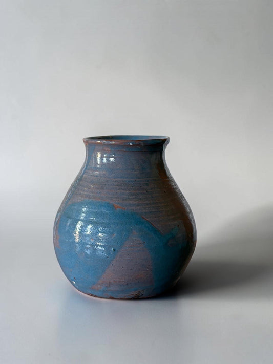 May include: A handmade ceramic vase with a rounded body and a narrow neck. The vase features a blend of blue and brown hues, with a textured surface and a glossy finish. The design includes a splash of blue paint.