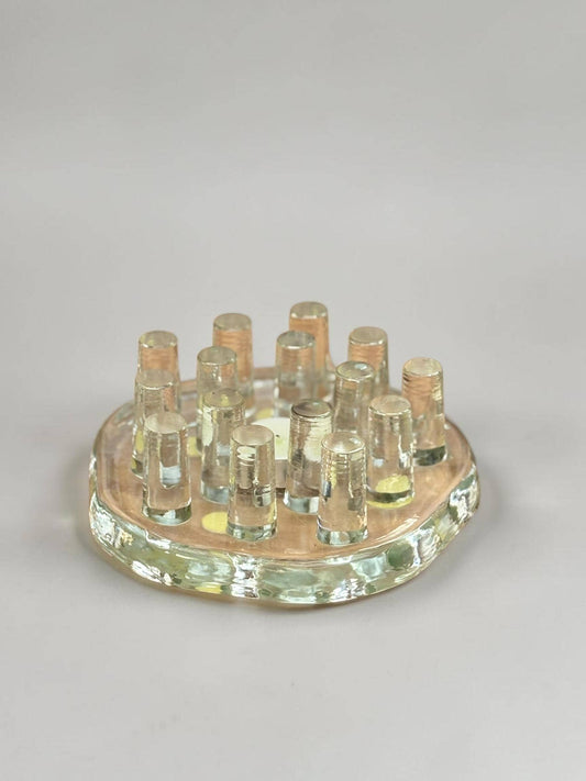 May include: A circular glass flower frog featuring a thick, textured base with a light amber tint. The piece includes twelve vertical, clear glass cylindrical tubes arranged in a grid pattern, designed to hold individual flower stems upright.